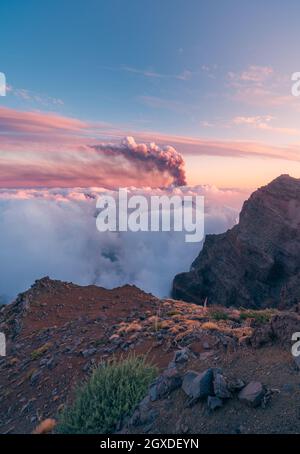 Alba su possenti vette di montagna tra morbide e folte nuvole bianche e sullo sfondo l'eruzione di un vulcano. Eruzione vulcanica di Cumbre Vieja a la Foto Stock