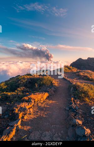 Alba su un sentiero di montagna ad alta quota tra morbide e spesse nuvole bianche e l'eruzione di un vulcano sullo sfondo. Cumbre Vieja eruzione vulcanica Foto Stock