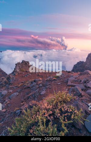 Alba su possenti vette di montagna tra morbide e folte nuvole bianche e sullo sfondo l'eruzione di un vulcano. Eruzione vulcanica di Cumbre Vieja a la Foto Stock