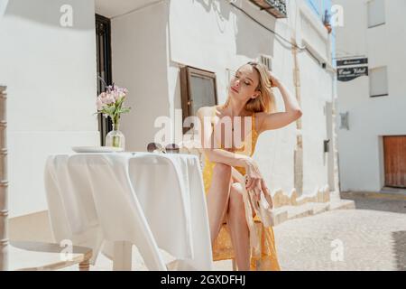Ballerina femminile tranquilla con occhi chiusi attaccando i capelli mentre si siede a tavola con gambe incrociate e scarpe a punta nella città vecchia Foto Stock