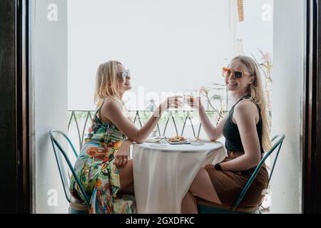 Vista laterale delle amiche felici che pranzano al tavolo e bicchieri di cocktail sul balcone Foto Stock