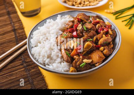 Da sopra composto ciotola con Kung pao pollo con arachidi di riso bianco e peperoncino rosso caldo e cipolla verde e bacchette Foto Stock