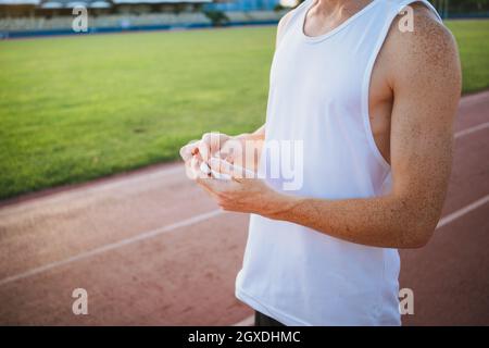 Ritagliate il giovane atleta maschile in una maglietta da indossare con gli auricolari mentre guardate lontano nello stadio Foto Stock