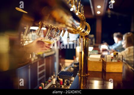 Il barista versa la birra fresca in un bicchiere. Amici svaghi al banco in bar, vita notturna. Gruppo di persone rilassarsi in pub, vita notturna, amicizia, Foto Stock