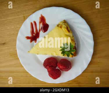 Cheescake affettare con 3 fragole e salsa di fragole in un piatto bianco. Vista dall'alto Foto Stock