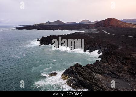 Vista del mare schiumoso contro la strada curva e le montagne con Hervideros in Yaiza Lanzarote Isole Canarie Spagna Foto Stock