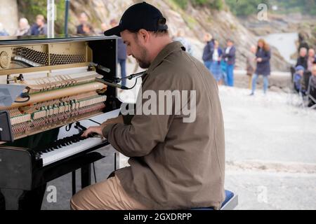 Il pianista e compositore contemporaneo Elliott Jacqués suona il pianoforte sulla spiaggia di Trebah Garden a Polgwidden Cove in Cornovaglia. Foto Stock