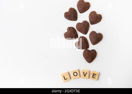 Caramelle al cioccolato al tartufo a forma di cuore su sfondo bianco. Iscrizione amore fatto di lettere di legno. Luogo per un'iscrizione Foto Stock