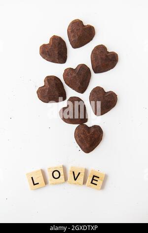 Caramelle al cioccolato al tartufo a forma di cuore su sfondo bianco. Iscrizione amore fatto di lettere di legno Foto Stock