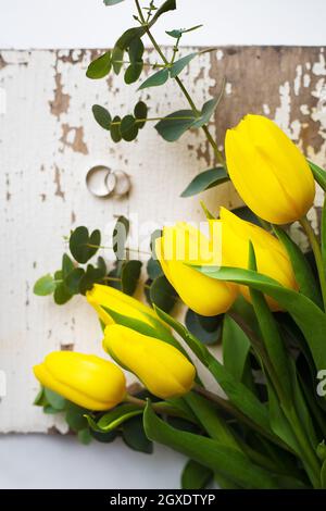 Bellissimi gli anelli di nozze con tulipani gialli sul vecchio tavolo bianco Foto Stock