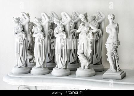 Collezione di varie statuette di marmo bianco souvenir di donne in stile antico tradizionale posto sul supporto contro la parete Foto Stock