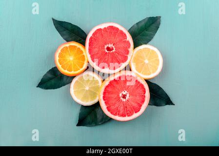 Vista dall'alto di fette di frutta colorate con disposizione a foglia di agrumi. Succo tropicale estivo con limone, pompelmo e arancio su tavola blu d'annata. Foto Stock