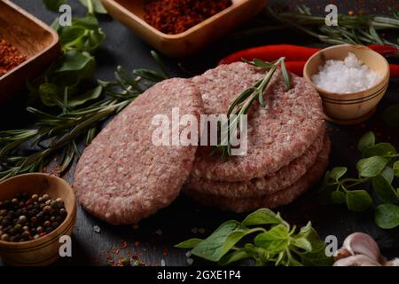 Hamburger di manzo crudo con erbe e spezie. Hamburger crudi su fondo di cemento Foto Stock