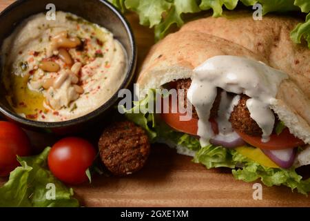 Falafel in pita pane con insalata di verdure, salsa harissa, humus, tahini su fondo di legno. Concetto di fast food mediorientale. Tradizionale israeliano f Foto Stock