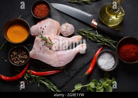 Quarti di pollo crudi, gambe con erbe e spezie pronte per grigliare su sfondo scuro. Foto Stock