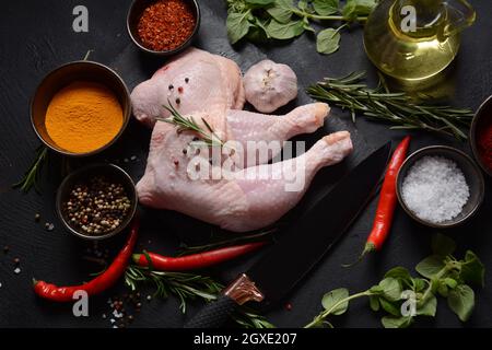 Quarti di pollo crudi, gambe con erbe e spezie pronte per grigliare su sfondo scuro. Foto Stock