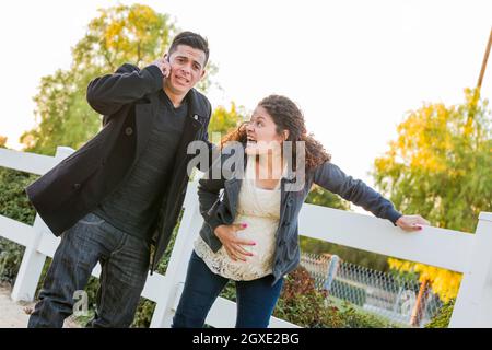 Donna incinta in dolore con la mano sul suo Belly mentre il marito usa il telefono delle cellule fuori. Foto Stock