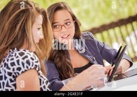 Attraente razza mista ragazze sorridenti e parlare mentre si lavora sul computer Tablet seduti all'aperto. Foto Stock