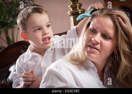 Cute Son spazzolando i capelli di sua mamma in interni. Foto Stock