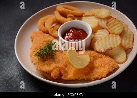 Schnitzel di carne e patate fritte con anelli di cipolla fritti, insalata di verdure Foto Stock