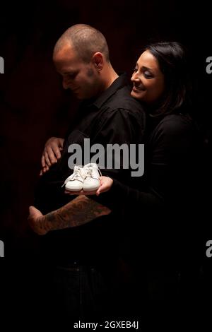 Divertimento razza mista Giovane Azienda Nuovi White scarpe per bambini contro uno sfondo nero sotto illuminazione drammatica. Foto Stock