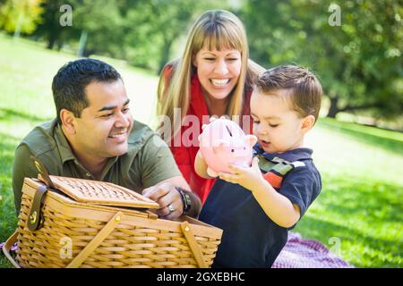 Felice razza mista giovane dare il loro figlio un salvadanaio ad un picnic nel parco. Foto Stock