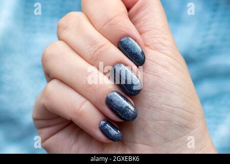 Mano femminile con bel manicure - chiodi blu scuro glittered su fondo tessuto maglia blu maglione. Messa a fuoco selettiva. Primo piano Foto Stock