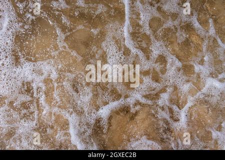 Lacy modello di onda e schiuma di mare che rotola sulla riva. Foto Stock