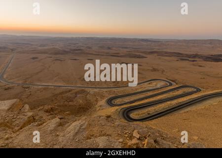 Alba vista di una strada tortuosa e il paesaggio di Makhtesh (cratere) Ramon, nel deserto del Negev, Israele meridionale. È una forma geologica di a la Foto Stock