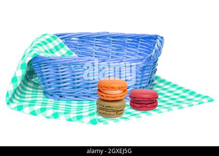 Closeup di un cesto di vimini vuoto e tre macaron su un tovagliolo bianco verde a scacchi, coperta o tovaglia isolato su uno sfondo bianco. Per la f Foto Stock