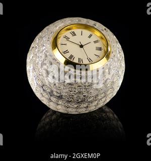 Un orologio a forma di palla da golf in cristallo con finiture in oro e quasi a tre ore isolato su uno sfondo nero puro. Foto Stock