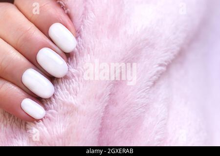 Mano femminile con bel manicure - chiodi bianchi in avorio su tessuto morbido rosa pallido, fondo tessile con spazio copia Foto Stock