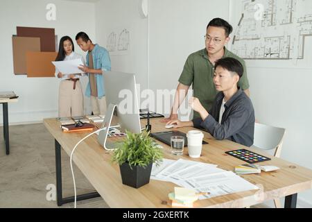 Due giovani designer di etnia asiatica che guardano lo schermo del computer sul posto di lavoro Foto Stock