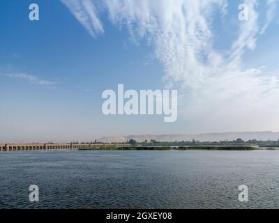 Il fiume Nilo in primo piano con Esna sbarramento all'orizzonte con lontano deserto catena montuosa dietro, Egitto, Africa Foto Stock