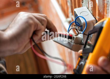 Vista dal basso. L'elettricista che lavora con il tester misura la tensione in un impianto elettrico. Industria edile. Foto Stock