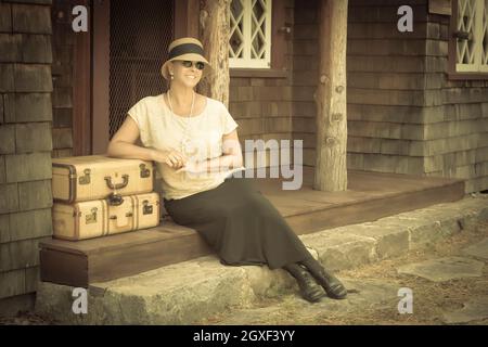 Piuttosto 1920s vestito girl accanto a valigie sul portico con effetto vintage aggiunto. Foto Stock