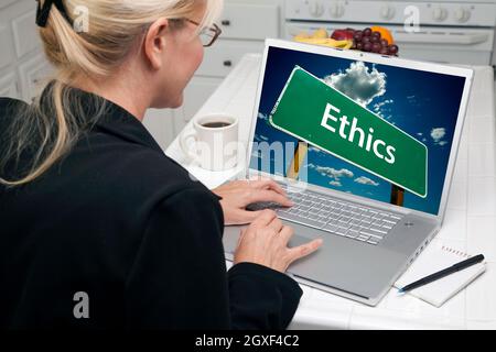 Donna in cucina che utilizza il laptop con lo schermo di accesso alla Ethics Road. Lo schermo può essere utilizzato facilmente per i propri messaggi o immagini. L'immagine sullo schermo è la mia copia Foto Stock