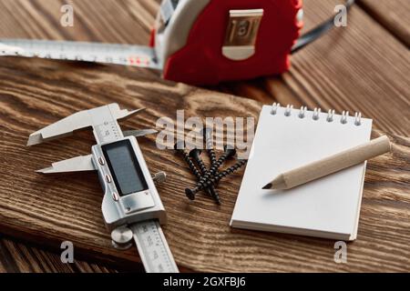 Nastro di misurazione, calibro e taccuino, vista macro, sfondo in legno, nessuno. Strumento professionale, attrezzatura da carpentiere o da costruttore, attrezzi da lavoro in legno Foto Stock