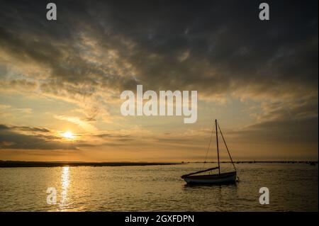 Cielo spettacolare con il sole che tramonta sulla costa del Mare del Nord vicino a Blakeney Point con barche in silhouette ormeggiate sull'acqua, Norfolk, Inghilterra. Foto Stock