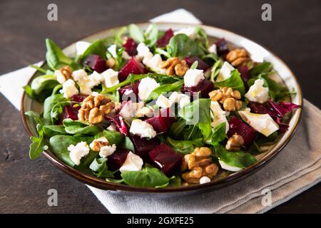Insalata di barbabietole o barbabietole con rucola fresca, formaggio morbido e noci sul piatto, condimento e spezie su sfondo di legno scuro, spazio copia, vista dall'alto/ Foto Stock