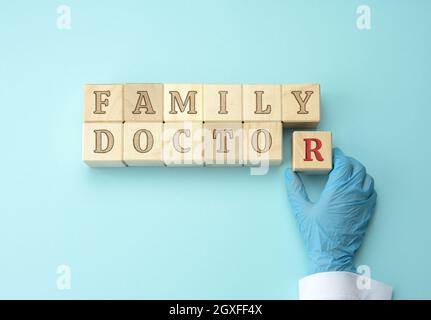 blocchi di legno con l'iscrizione medico di famiglia e una mano del medico in un guanto di lattice blu. Concetto di firma di una dichiarazione medica, assicurazione Foto Stock