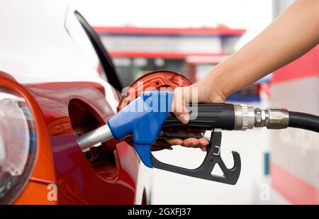 La mano del lavoratore della stazione di benzina che tiene la pompa blu del gas del benzene, riempiendo il serbatoio rosso dell'automobile di sport. Primo piano Foto Stock