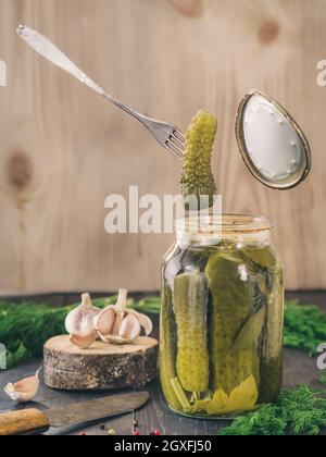 La forcella può contenere un cetriolo sottaceto che appena è stato preso da un barattolo di vetro. Cetrioli sottaceto su sfondo di legno. Sottaceti in un barattolo di vetro con aglio, p Foto Stock