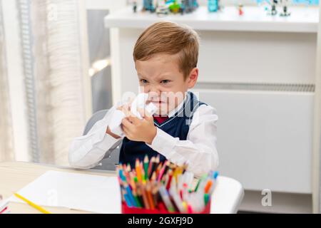 Carino ragazzo prima livellatore in uniforme scuola a casa durante una pausa folgorante mentre si siede alla sua scrivania. Messa a fuoco selettiva. Primo piano. Verticale Foto Stock