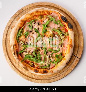 Vista dall'alto della pizza calda su un piedistallo in legno. Pizza Capricciosa , base di pomodoro. Tenere il prosciutto, i funghi, le olive e l'rucola fresca a base di due chee Foto Stock