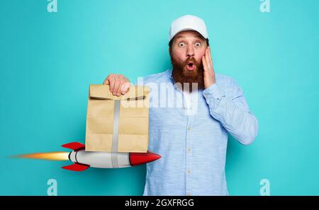 Deliveryman con l'espressione domandata pronto a trasportare il sacchetto veloce con il cibo come un razzo. Foto Stock