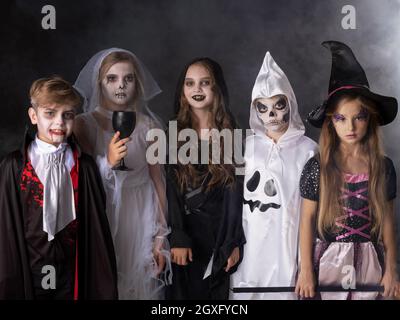 Buon Halloween partito con i bambini trucco o trattando in diversi costumi fantasma, vampiro, scheletro, strega Foto Stock