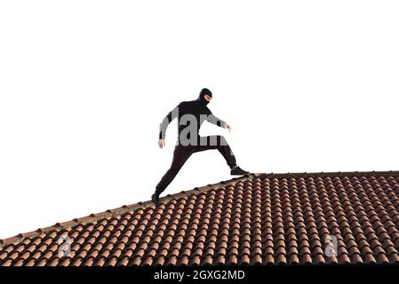 Ladro vestito di nero camminando sul tetto di una casa Foto Stock