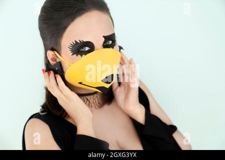 Ragazza con trucco halloween e maschera medica arancione sul viso. Halloween durante il coronavirus. Foto Stock