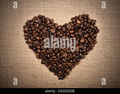 Sfondo di chicchi di caffè a forma di cuore su sfondo burlap Foto Stock
